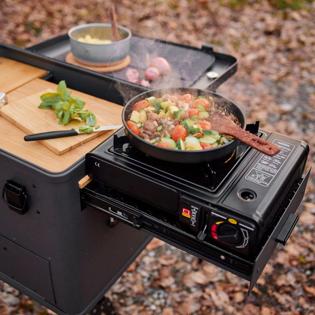Layzee Kitchenbox mit seitlichem Auszug und Gaskocher mit Gemüsepfanne, Schneidebrett und Deckel als Tisch.