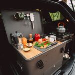 Campingküche Layzee Kitchenbox mit Gemüse im Kofferraum eines Autos.